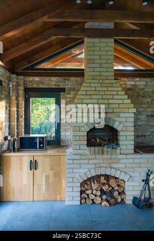 Caminetto interno rustico con camino in mattoni e deposito in legno, a creare un'atmosfera invitante. Foto Stock