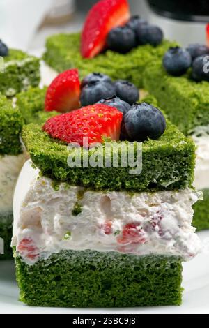 Uno strato verde di pan di Spagna ricoperto di panna montata, mirtilli e fragole. Foto Stock