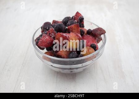 Frutti e bacche miscelati surgelati in una ciotola di vetro su fondo di legno. Foto Stock