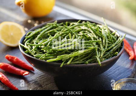 Una ciotola di Salicornia verde fresca o alghe di Samphire su un tavolo con limone, olio e peperoncino Foto Stock