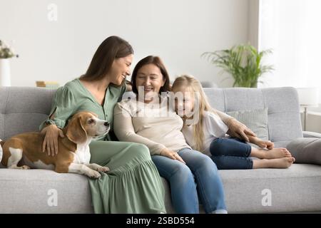 Tre generazioni di donne si siedono vicino sul divano con il cane Foto Stock
