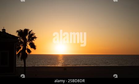Un incantevole tramonto a Venice Beach, California, con il sole dorato che scende oltre l'orizzonte, illuminando l'Oceano Pacifico in un tono ricco e caldo Foto Stock
