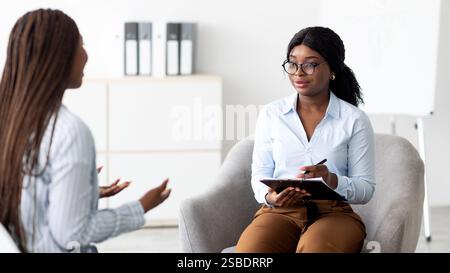 Amichevole psicologa afroamericana che ha una sessione con cliente femminile in ufficio. Consulenza psicoterapeutica Foto Stock