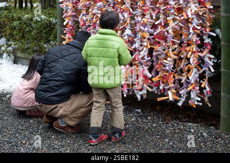 Persone che legano il loro "omikuji" (oracolo di carta di buona o cattiva fortuna) a una stringa durante "Hatsumode" (visita al santuario di Capodanno) a Taga Taisha, Hikone, Giappone. Foto Stock