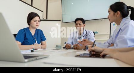 Team sanitario diversificato impegnato in una riunione seria per definire le strategie di assistenza ai pazienti. Foto Stock