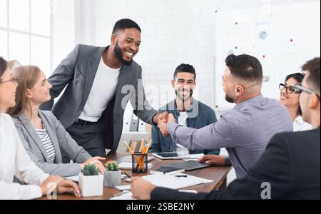 Due uomini d'affari che stringono la mano, seduti alla scrivania Foto Stock
