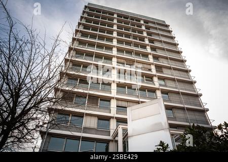 Una torre di uffici a più piani degli anni '1970 si erge sopra gli alberi circostanti, mostrando un design ripetitivo in cemento e grandi finestre. Questo buildi urbano Foto Stock