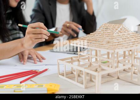 Architetto che spiega il piano di progetto ai clienti. Donna d'affari sicura che ha un modello architettonico in ufficio, modello strutturale casa. Dati funzionanti e. Foto Stock