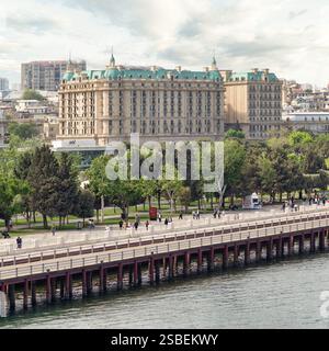 Baku, Azerbaigian - 4 maggio 2024: I visitatori passeggiano lungo il lungomare sul Mar Caspio con alberi lussureggianti che costeggiano i passaggi pedonali vicino all'hotel Four Seasons in una bella giornata Foto Stock