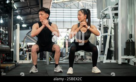 Una coppia asiatica sportiva e atletica di abbigliamento sportivo si allena insieme in palestra, eseguendo squat ed esercizi di peso corporeo. concetto di stile di vita sano Foto Stock