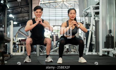 Una coppia asiatica sportiva e atletica di abbigliamento sportivo si allena insieme in palestra, eseguendo squat ed esercizi di peso corporeo. concetto di stile di vita sano Foto Stock