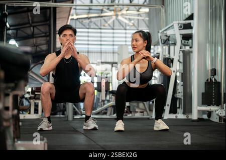 Una coppia asiatica sportiva e atletica di abbigliamento sportivo si allena insieme in palestra, eseguendo squat ed esercizi di peso corporeo. concetto di stile di vita sano Foto Stock