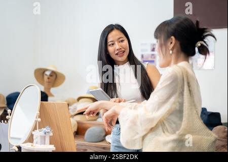 Un'amichevole e bella dipendente asiatica del negozio sta aiutando un cliente a provare un braccialetto, facendo una buona conversazione per assicurarsi che abbia un piacevole intrattenimento Foto Stock