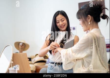Un'amichevole e bella dipendente asiatica del negozio sta aiutando un cliente a provare un braccialetto, facendo una buona conversazione per assicurarsi che abbia un piacevole intrattenimento Foto Stock