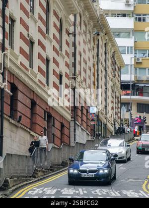 Hong Kong, Cina - 1 febbraio 2025: Una vista ravvicinata di una strada stretta e ripida nel quartiere centrale degli affari di Hong Kong. Le auto salgono in pendenza, S. Foto Stock