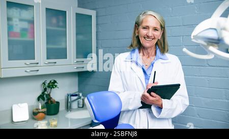 Dentista donna sorridente nel moderno ufficio dentale con tablet Foto Stock