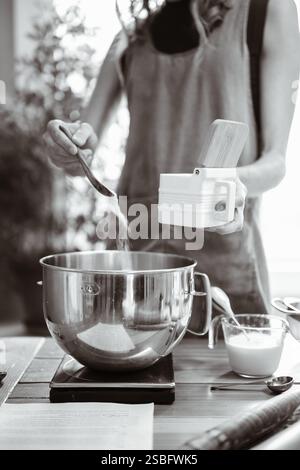 Panettiera artigianale aggiunta di ingredienti al recipiente per la preparazione del pane Foto Stock