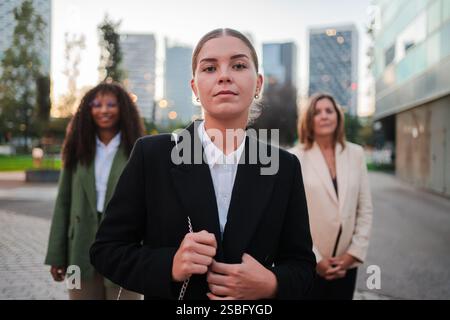 Gruppo di donne del lavoro fiduciose in piedi insieme, mostrando empowerment e professionalità nelle loro espressioni determinate e posture avvolte mentre si impegnano in conversazioni importanti. Foto di alta qualità Foto Stock