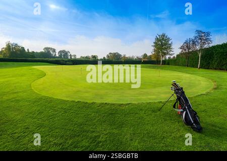 Borsa da golf con diversi club in piedi su un putting green perfettamente falciato all'interno di un campo da golf, pronti per l'allenamento di un golfista Foto Stock