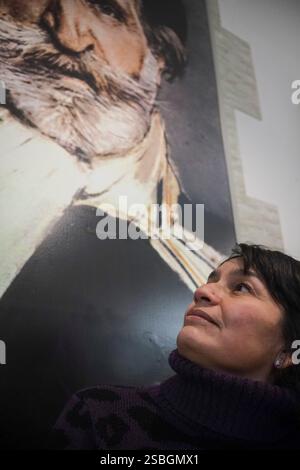 Una donna guarda verso l'alto un grande ritratto di un uomo anziano distinto, perso nel pensiero. Foto Stock