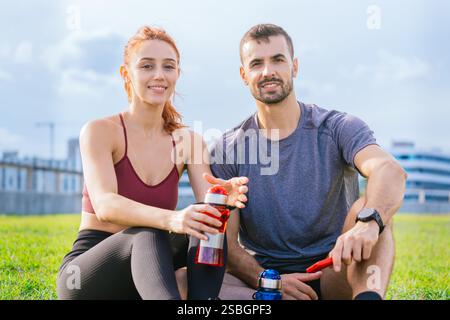 Coppia in forma sorridente che riposa all'aperto dopo l'allenamento con una bevanda rinfrescante Foto Stock