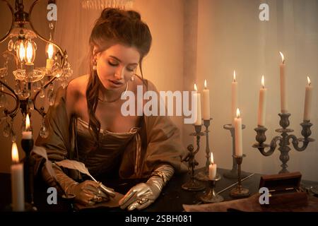 Una giovane donna in costume da vampiro scrive con attenzione a lume di candela, avvolta nel mistero. Foto Stock