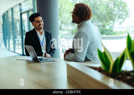 Due colleghi sono felici di chattare in un ambiente professionale con luce naturale e vegetazione, migliorando la creatività e il comfort. Un notebook sul d Foto Stock