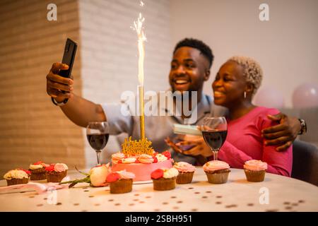 Felice giovane coppia che festeggia il compleanno della donna a casa. Stanno abbracciando e facendo selfie. Foto Stock