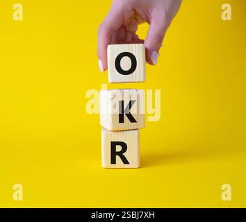 Obiettivi OKR e simbolo dei risultati chiave. Cubi in legno con parole obiettivi OKR e risultati chiave. Mano d'affari. Bellissimo sfondo giallo. Affari Foto Stock