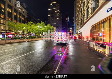 Ambulanza FDNY con luci lampeggianti sulla bagnata Manhattan Street di notte, che si riflette sul marciapiede vicino all'ingresso della metropolitana. New York. STATI UNITI. Foto Stock