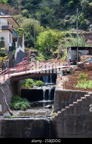 Letto di fiume in cemento. Scala e piccolo ponte. Casa e montagna con vegetazione fresca sullo sfondo. Sao Vicente, Madeira, Portogallo. Foto Stock
