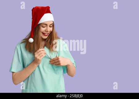Ritratto di una giovane dentista femminile nel cappello di Babbo Natale con attrezzi su sfondo viola Foto Stock