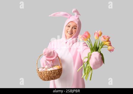 Divertente donna anziana in costume da coniglietto con cesto con uova di Pasqua e tulipani su sfondo bianco Foto Stock