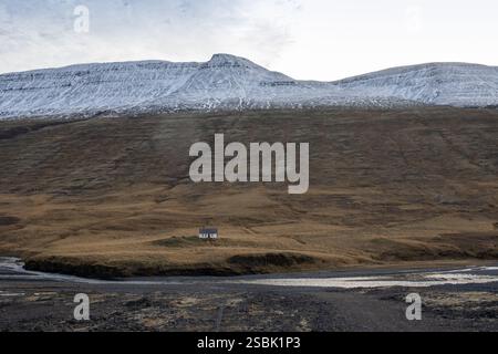 Montagne maestose coperte da erba, muschio e licheni e più in alto con neve. Piccola vecchia casa accanto ad un fiume quasi secco. Cielo nuvoloso. Islanda settentrionale. Foto Stock