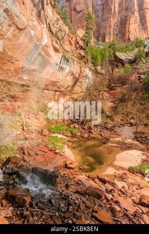 Un piccolo flusso d'acqua scorre lungo una collina rocciosa. L'acqua è limpida e le rocce sono marroni Foto Stock