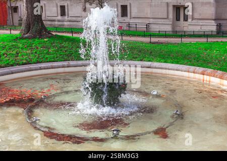 La piccola fontana di Parigi presenta acqua che sgorga da una struttura centrale in pietra, circondata da un bacino circolare con luci sommerse. Fountain è incastonata i Foto Stock