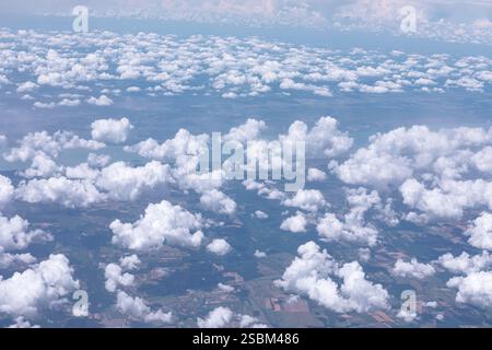 Vista a volo d'uccello di un paesaggio con una dispersione di soffici nuvole bianche nel cielo. Il terreno sottostante presenta macchie di terra in varie tonalità che indicano Foto Stock