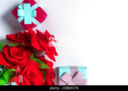 Vista dall'alto di eleganti confezioni regalo e rose rosse vivaci su sfondo bianco. Perfetto per celebrare l'amore, le occasioni speciali o per esprimere gratitudine. Foto Stock