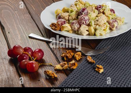 Una rinfrescante insalata di pollo combina uva succosa, gambi di sedano croccanti e salsa cremosa di yogurt, splendidamente disposta su un piatto bianco. Nelle vicinanze ci sono Foto Stock