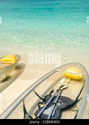 Kayak trasparenti su una spiaggia tropicale con acque turchesi Una tranquilla spiaggia tropicale con tre kayak trasparenti su soffice sabbia bianca, sopra Foto Stock