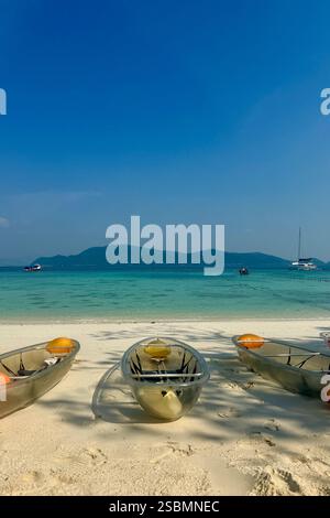 Kayak trasparenti su una spiaggia tropicale con acque turchesi Una tranquilla spiaggia tropicale con tre kayak trasparenti su soffice sabbia bianca, sopra Foto Stock