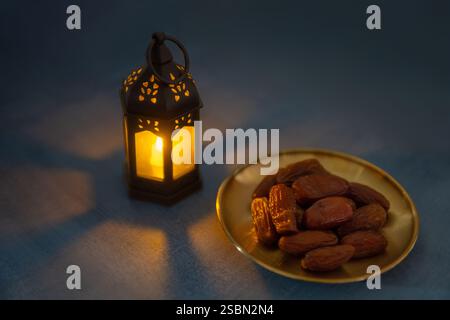 Una lanterna illuminata che proietta un caldo bagliore su un piatto di datteri su uno sfondo scuro. Concetto di Ramadan Kareem. Foto Stock