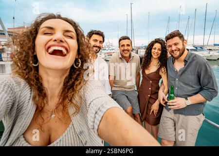 Gruppo di amici allegri che si fanno un selfie su una barca al porticciolo, si godono una vacanza estiva e celebrano l'amicizia. Foto Stock