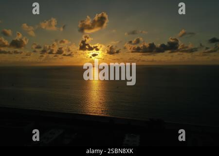 Una vista mozzafiato del sole che tramonta sull'oceano, che getta riflessi dorati sull'acqua, circondati da morbide nuvole nel cielo serale. Foto Stock