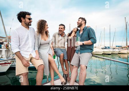 Un gruppo di amici allegri che si godono una divertente gita in yacht in un porticciolo. Rilassate vibrazioni delle vacanze estive, risate e connessione in un'avventura in barca a vela. Ven Foto Stock