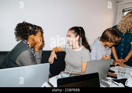 Felici amici femminili multirazziali che pettegolezzano mentre sono seduti nel dormitorio del college Foto Stock