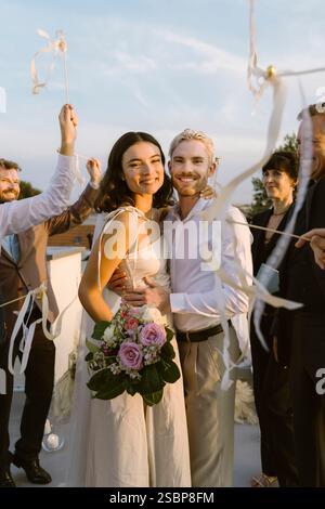 Ritratto della sposa e dello sposo felici in piedi con le braccia l'uno intorno all'altro durante la festa sul tetto Foto Stock