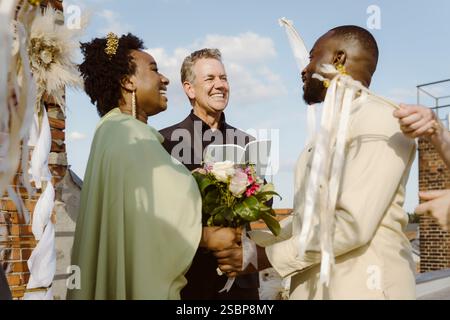 Sorridente anziano ministro che guarda la coppia appena sposata alla cerimonia Foto Stock
