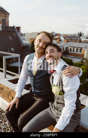 Ritratto di una coppia gay sposata sorridente seduta insieme sul tetto Foto Stock