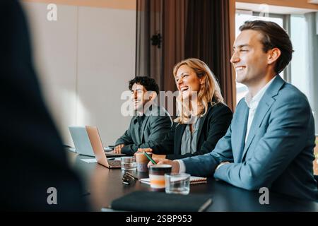 Felice imprenditore multirazziale maschio e femmina che ridono durante la riunione del Consiglio in ufficio Foto Stock